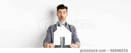Real estate and insurance concept. Excited man showing paper house cutout and say wow, checking out apartment or property, standing amazed on white background 98896016