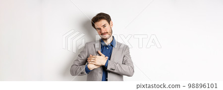 Romantic handsome guy with beard holding hands on heart and smiling, thanking you, feeling nostalgic, having tender memories in heart, white background 98896101
