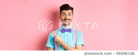 Handsome caucasian guy with bristle and moustache pointing finger right aside, showing advertisement, standing over pink background in classy bow-tie Handsome caucasian guy with bristle and moustache pointing finger right aside, showing advertisement, standing over pink background in classy bow-tie 98896186