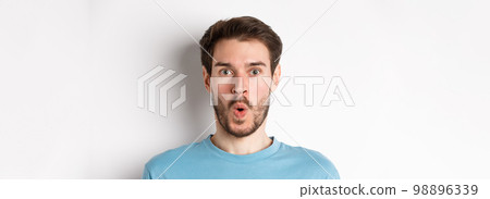 Close-up of surprised man face, saying wow and staring at camera amazed, standing on white background Close-up of surprised man face, saying wow and staring at camera amazed, standing on white background 98896339