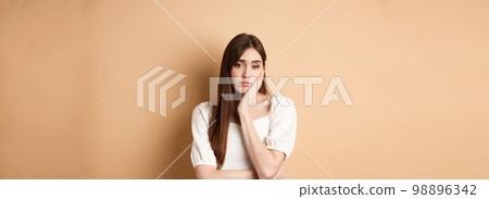 Bored and tired young woman looking indifferent at camera, lean face on palm and stare at camera unamused, standing sleepy on beige background Bored and tired young woman looking indifferent at camera, lean face on palm and stare at camera unamused, standing sleepy on beige background 98896342