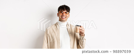 Real people. Happy young man drinking coffee from paper cup, order takeaway at favourite cafe, smiling and looking pleased at camera, white background 98897039