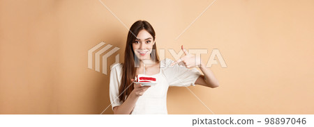 Cute girl pointing at birthday cake with candle and smiling excited, making bday wish, standing on beige background Cute girl pointing at birthday cake with candle and smiling excited, making bday wish, standing on beige background 98897046