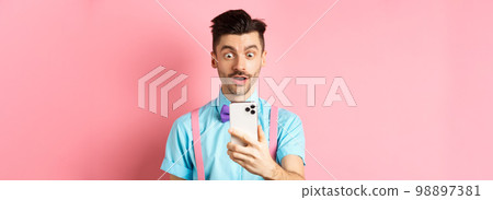 Impressed man reading mobile screen with amazed face, seeing online promo offer, standing over pink background Impressed man reading mobile screen with amazed face, seeing online promo offer, standing over pink background 98897381