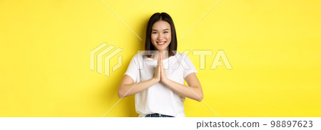 Beautiful asian woman say thank you, holding hands in namaste, pray gesture and smiling, being grateful, standing over yellow background Beautiful asian woman say thank you, holding hands in namaste, pray gesture and smiling, being grateful, standing over yellow background 98897623