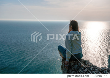 A young tourist Woman enjoying sunset over sea mountain landscape while sitting outdoor. Women's yoga fitness routine. Healthy lifestyle, harmony and meditation 98898136