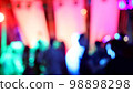 Blurred silhouettes of crowd of people dancing on the dance floor of a night club under the light of colored spotlights and lasers. 98898298