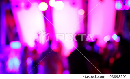 Blurred silhouettes of crowd of people dancing on the dance floor of a night club under the light of colored spotlights and lasers. 98898301