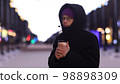 Young handsome man in glasses is walking in city in winter, drinking hot tea or coffee from paper cup 98898309