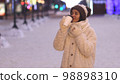 Winter portrait of a young woman in warm clothing warming herself with a hot drink. 98898310
