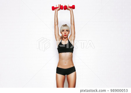Front view of sportive blonde beautiful woman lifting up red dumbbells isolated on white background 98900053