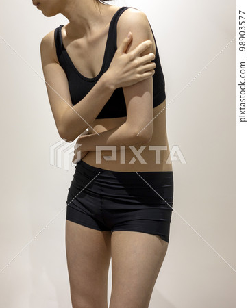 一位身穿黑色運動服、雙手摀住手臂和腹部的女性的正面圖 98903577
