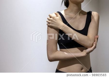 Front view of woman covering shoulders and elbows with hands while wearing black sportswear 98903583