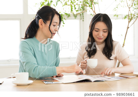 Two women consulting while looking at a pamphlet Two women consulting while looking at a pamphlet 98903661