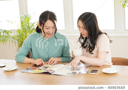 Two women consulting while looking at a pamphlet Two women consulting while looking at a pamphlet 98903689