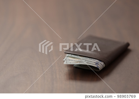 Full grain leather wallet with us dollars on walnut table 98903769