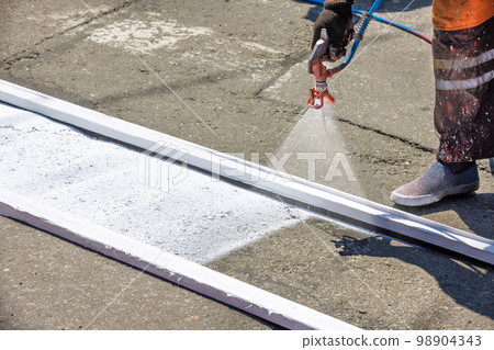 A road worker applies white road markings to a pedestrian crossing. 98904343