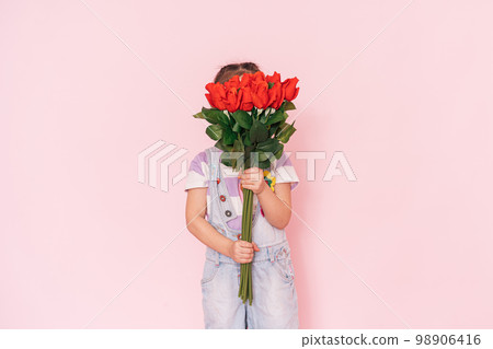 Little girl in overalls holding bouquet of roses against pink background 98906416