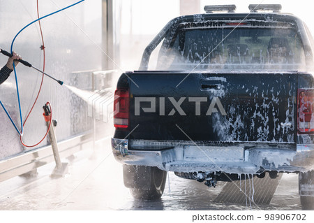 Process of man washing his car in a self-service car wash station. Back view Process of man washing his car in a self-service car wash station. Back view 98906702