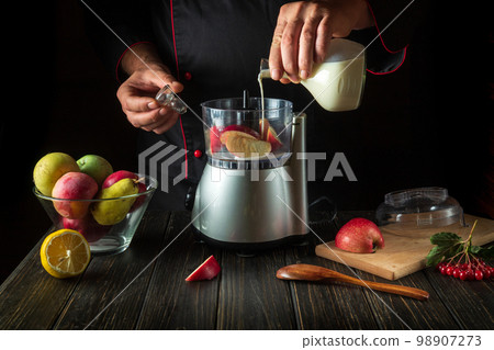 The chef prepares a fruit cocktail with milk. The idea of a fruit diet for breakfast in the morning. Menu concept for hotel on dark background The chef prepares a fruit cocktail with milk. The idea of a fruit diet for breakfast in the morning. Menu concept for hotel on dark background 98907273