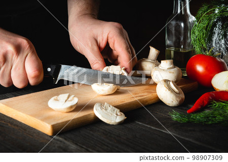 The chef cuts mushrooms with knife to prepare delicious food. Set of vegetables on a vintage kitchen table in a restaurant or cafe. Delicious recipe for breakfast or lunch The chef cuts mushrooms with knife to prepare delicious food. Set of vegetables on a vintage kitchen table in a restaurant or cafe. Delicious recipe for breakfast or lunch 98907309