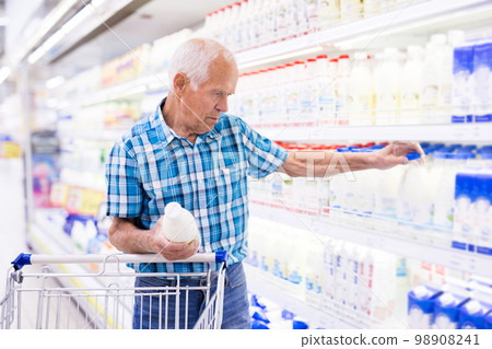 elderly retired man buying milk in dairy section of the supermarket 98908241