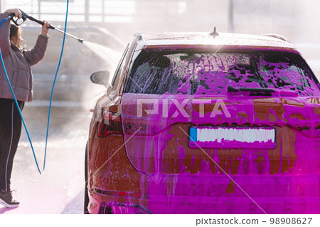 Young woman cleaning her car with a jet sprayer. Self-service car washing. Orange auto Young woman cleaning her car with a jet sprayer. Self-service car washing. Orange auto 98908627