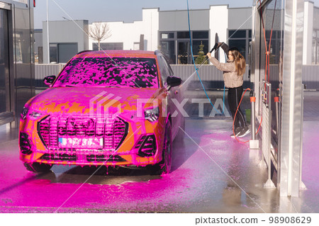 Young woman cleaning her car with a jet sprayer. Self-service car washing. Orange auto 98908629
