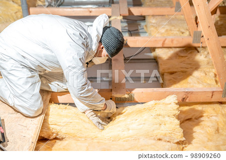 man insulates the roof and ceiling of the house with glass wool man insulates the roof and ceiling of the house with glass wool 98909260