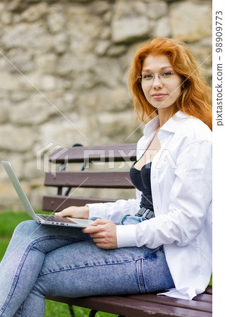 Young attractive redhead girl using the laptop looking straight into the camera 98909773