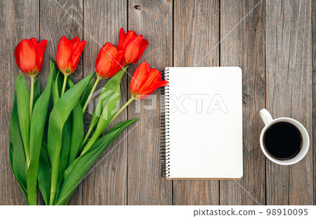 Bouquet of red tulips, cup of coffee and notebook on a wooden background. 98910095