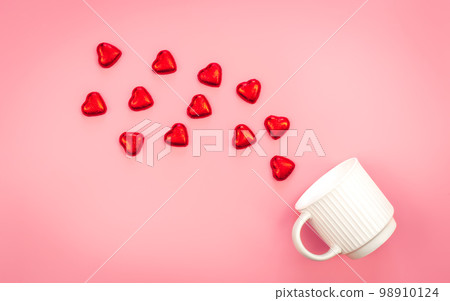 A cup and scattered heart-shaped sweets on a pink background, flat lay. 98910124