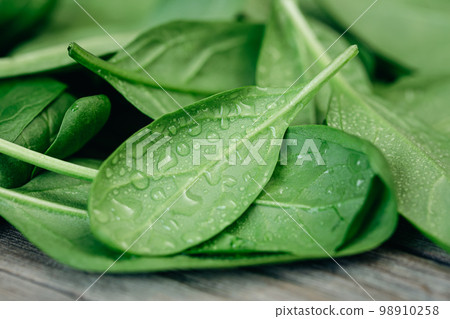 Wet fresh green baby spinach leaves on a wooden background. Wet fresh green baby spinach leaves on a wooden background. 98910258