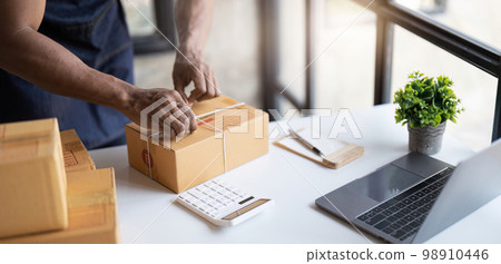 Young start up small business owner writing address on cardboard box at workplace.small business entrepreneur SME , working with box at home, Online selling, e-commerce, packing concept 98910446