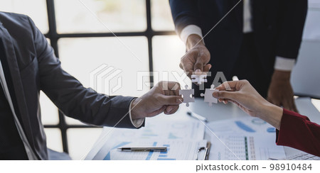 Business people with jigsaw puzzle pieces in office, Successful teamwork and partnership concept. hands holding pieces of white jigsaw puzzle 98910484