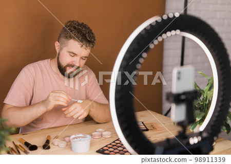 Male beauty blogger with makeup product recording video at home. Using ring lamp and smartphone. Vlog cosmetic products and diversity concept 98911339