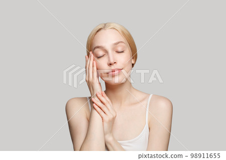 Portrait of blonde gorgeous woman with clean skin touching her face isolated on grey background. 98911655