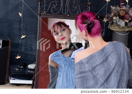 teenager girl looks in the mirror indoor while trying on a dress teenager girl looks in the mirror indoor while trying on a dress 98912134