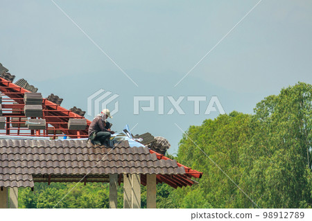 Construction roofer installing roof tiles at house building site Construction roofer installing roof tiles at house building site 98912789