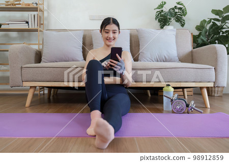 Healthy asian woman practicing relaxation yoga at home. Spending time and playing phone at home concept Healthy asian woman practicing relaxation yoga at home. Spending time and playing phone at home concept 98912859