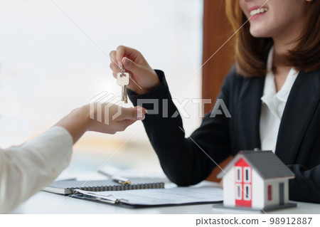 The real estate agent or agency giving house key to customer after signing agreement contract. Property concept. The real estate agent or agency giving house key to customer after signing agreement contract. Property concept. 98912887