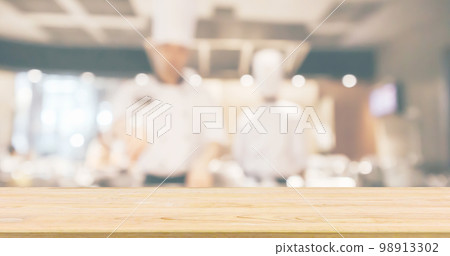 Empty Wood table top with Chef cooking in restaurant kitchen blurred defocused background 98913302