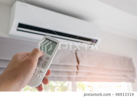 Hand with remote control directed on air conditioner 98913319