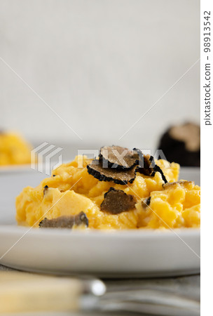 Scrambled eggs with fresh black truffles from Italy served in a plate close up, gourmet breakfast 98913542