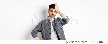 Annoyed young man looking tired or bothered, roll eyes and slap forehead, making facepalm from something stupid, standing on white background 98913870
