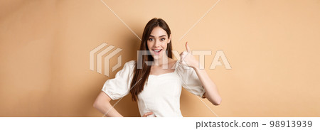 Amazed young woman showing thumb up, say yes and praise great product, approve choice, standing satisfied on beige background Amazed young woman showing thumb up, say yes and praise great product, approve choice, standing satisfied on beige background 98913939