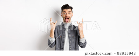 Excited funny guy showing tongue and heavy metal horns sign, enjoying party or event, having fun, standing on white background Excited funny guy showing tongue and heavy metal horns sign, enjoying party or event, having fun, standing on white background 98913948