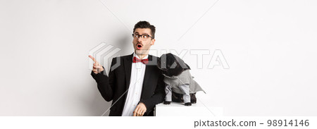 Animals, party and celebration concept. Amazed young man and black dog in costumes staring right at copy space, standing against white background Animals, party and celebration concept. Amazed young man and black dog in costumes staring right at copy space, standing against white background 98914146
