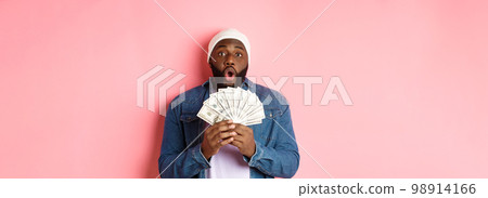 Amazed african-american man receive cash prize, showing money and staring at camera in awe, standing over pink background Amazed african-american man receive cash prize, showing money and staring at camera in awe, standing over pink background 98914166