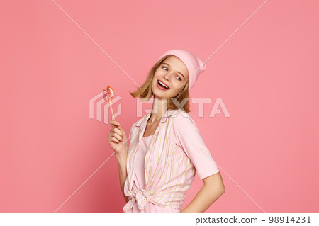 blonde woman holding candy on pink background. 98914231